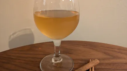 Cinnamon and apple mead in a small wine glas and two cinnamon sticks.