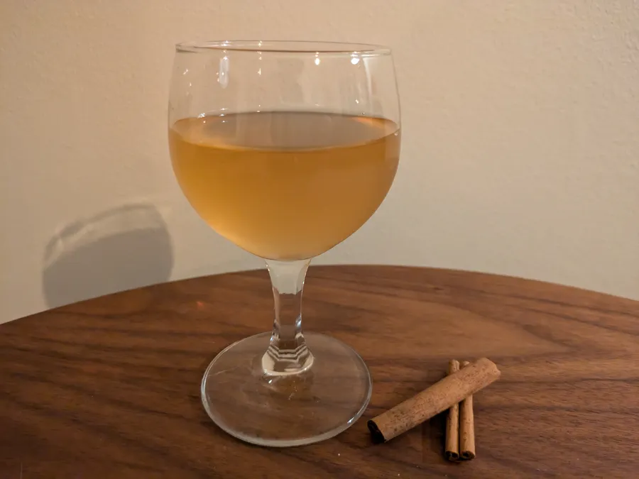 Cinnamon and apple mead in a small wine glas and two cinnamon sticks.