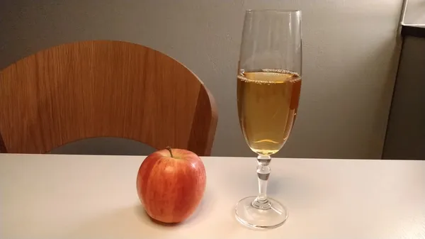 A glass of apple mead, cyser, and a red apple next to it.