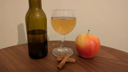 Cinnamon and apple mead in a small wine glass and a apple and two cinnamon sticks.