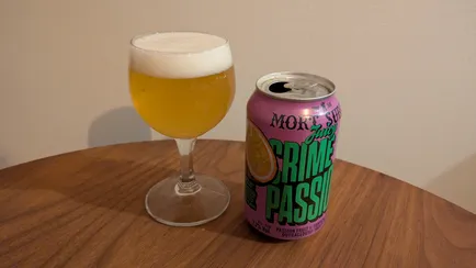 A can of "Juicy Crime of Passion" by Mort Subite to the right of a small wine glass filled with beer.