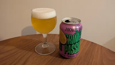 A can of "Juicy Crime of Passion" by Mort Subite to the right of a small wine glass filled with beer.